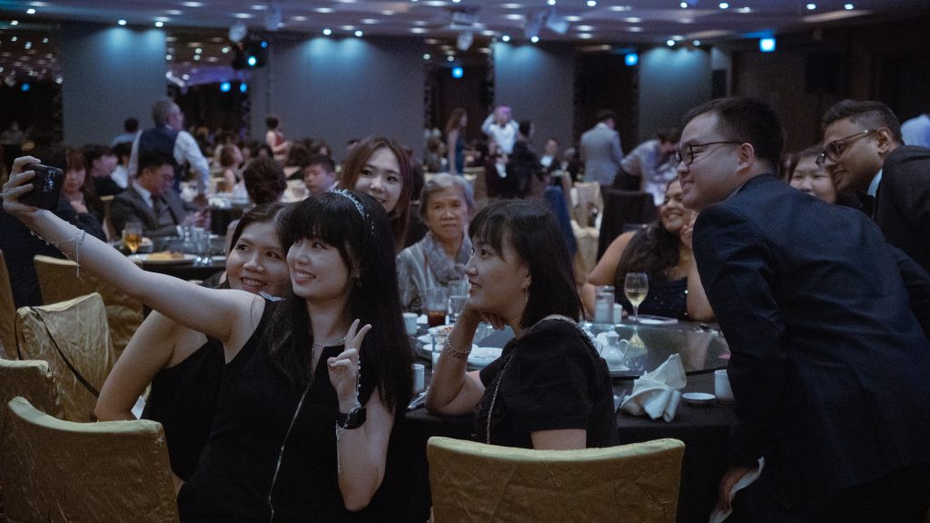 Corporate event guests enjoying and taking selfies during dinner function in Singapore